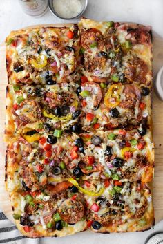 a square pizza on a cutting board with olives, peppers, and meatballs