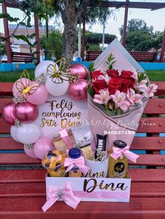 a valentine's day gift basket sits on a park bench with balloons and flowers