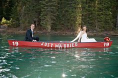 a bride and groom in a red canoe on the water with pine trees behind them