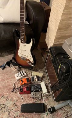 an electric guitar, amp and other electronics are on the floor next to a bed