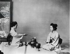 two women in kimonos are sitting on the floor and one is holding a teapot