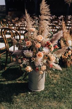 an arrangement of flowers in a bucket on the grass at a wedding ceremony with rows of chairs