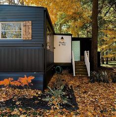 a small house in the woods with leaves on the ground