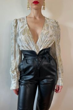 It's all couture and all mystery for the woman wearing this soft seducing silver and pearlescent wrap blouse. For maximum luxury; style with minimal makeup, a trademark red lip, and our Museum by Miss Gray couture Legacy Leather Pant. Fabric: Rayon, metallic Colour: Ivory, silver, gold Measurements: Chest 40", Waist 27", Length 21" Garment Care: Dry clean only Model: Height 5'7" - Chest 34", Waist 25", Hip 36.5" ⚜️⚜️⚜️ 10% surcharge on Etsy compared to our website due to fees 20% OFF at missgray Glamorous Formal V-neck Blouse, Luxury Gold Top For Evening, Luxury Gold Tops For Evening, Glamorous V-neck Blouse, Vintage V-neck Party Blouse, Glamorous V-neck Formal Blouse, Vintage V-neck Blouse For Party, Glamorous V-neck Blouse For Formal Occasions, Elegant Sequined Blouse For Spring