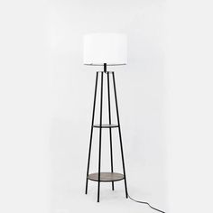 a floor lamp with a white shade on the top and a black stand underneath it