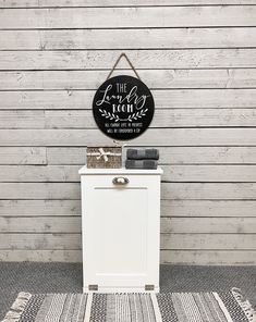 a white cabinet sitting on top of a rug next to a wooden wall with a sign above it