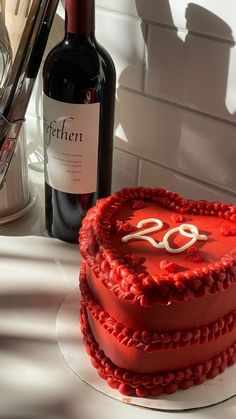 a red heart shaped cake sitting on top of a table next to a bottle of wine