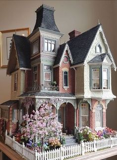 a large doll house on top of a wooden table with flowers in the front yard