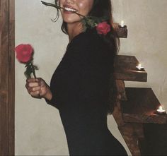 a woman holding two roses in front of her face with candles on the wall behind her