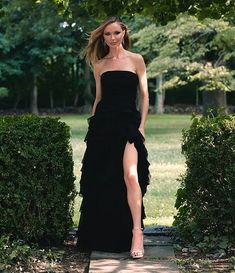 a woman in a black dress walking down a sidewalk