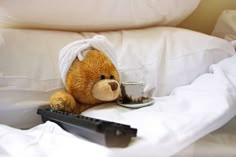 a teddy bear sitting on top of a bed next to a remote control and cup