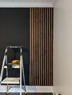 a ladder is in front of a black wall with vertical striped drapes on it