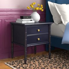 a night stand with two drawers in front of a purple wall and blue bedding