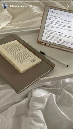 an open book sitting on top of a bed next to a tablet computer and pen