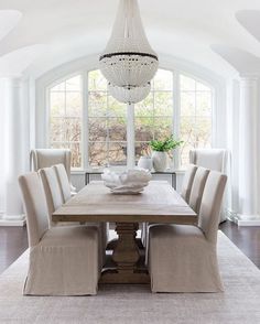 a dining room table with beige chairs and a chandelier hanging from the ceiling