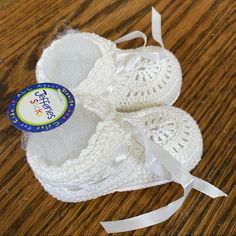 a pair of white crocheted baby booties on a wooden table with a ribbon