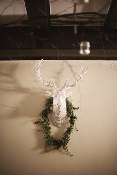 a deer head mounted to the side of a wall with greenery around it's antlers