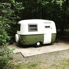 an old camper trailer is parked in front of some trees and bushes on a concrete slab