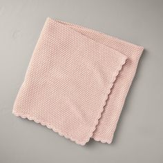 a pink blanket with scalloped edges on a gray surface