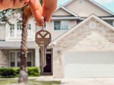 a hand holding a house key in front of a home