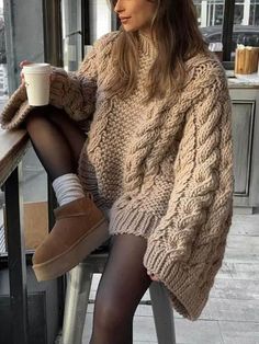 a woman is sitting on a chair with her legs crossed and holding a coffee cup