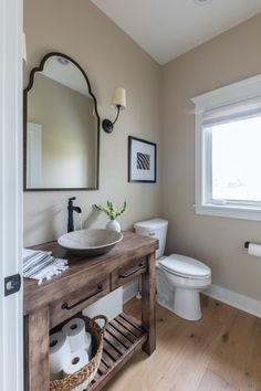 a white toilet sitting next to a bathroom sink under a mirror on top of a wooden counter