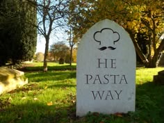 a sign that says he pasta way in front of some grass and trees with yellow leaves