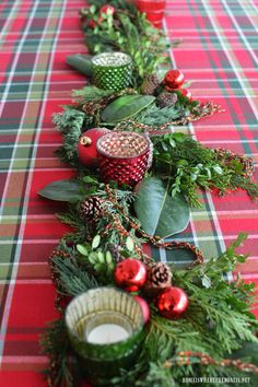 a christmas table runner with pine cones, greenery and red balls on the top