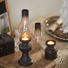 two lit candles are sitting on a wooden table next to an antique suitcase and other items