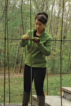 a woman standing in front of a metal fence with her hands wrapped around the pole