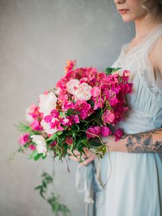 a woman in a white dress holding a bouquet of pink and white flowers with tattoos on her arm