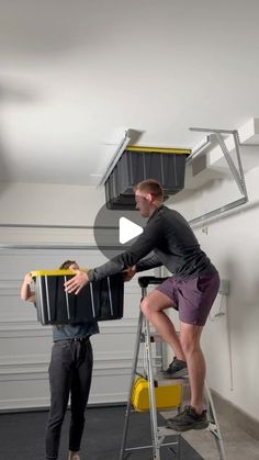 two men are standing on a ladder and one is holding a box