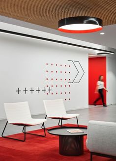 a woman walking through an office with red walls and white chairs in the foreground