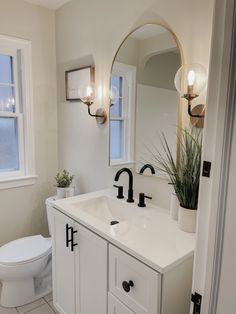 a bathroom with a toilet, sink and mirror in it's corner area next to a potted plant