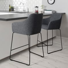 two gray chairs sitting on top of a counter next to a white kitchen island with a clock above it