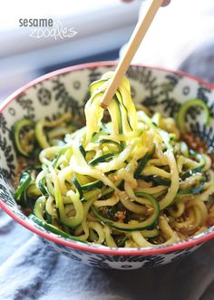 someone is holding a wooden spoon over a bowl of noodles with zucchini and spinach