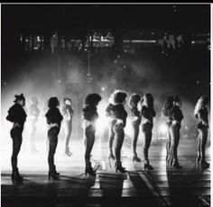 a group of women standing on top of a stage in front of a crowd at night