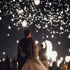 a bride and groom standing in front of floating lanterns at night with their backs to the camera