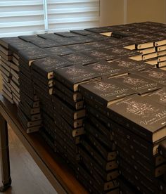 a stack of black books sitting on top of a wooden table next to a window