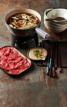 an assortment of food including meat, rice and chopsticks on a wooden table