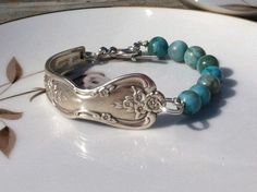 a silver bracelet with blue beads and flowers on it sitting on a white plate next to a flower