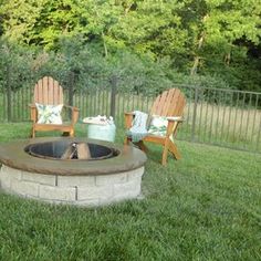 an outdoor fire pit with chairs around it in the middle of a grassy area next to a fence