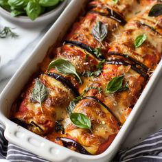 a white casserole dish filled with lasagna and basil garnish