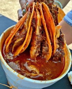 a person holding up some food in a bowl filled with sauce and tortilla chips