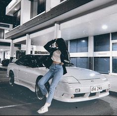 a woman sitting on the hood of a car in front of a building with windows