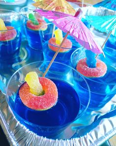 small desserts are arranged in clear bowls with umbrellas on the top and blue water