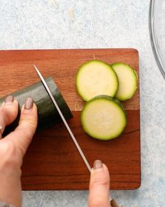 a person cutting cucumbers on a wooden cutting board