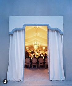 an open door to a dining room with white curtains and chandelier hanging from the ceiling