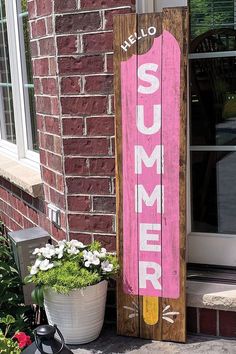 a wooden sign sitting on the side of a building next to a potted plant