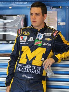 a man leaning against a wall wearing a racing suit